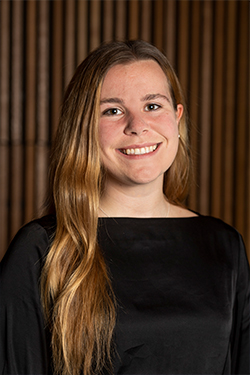Close up portrait photo of a smiling Sophie Young wearing a black long sleeve shirt. Sophie has long strawberry blonde hair and is wearing it to one side. .