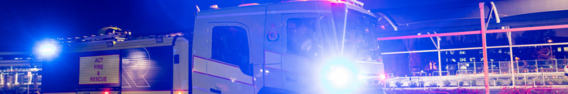 Fire and Rescue truck parked at night with flashing blue and red lights outside a brightly lit building