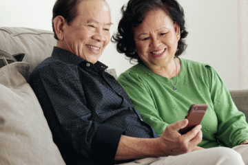 man and woman sitting on a couch looking at a mobile phone