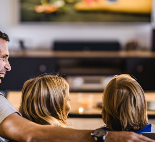 Family of mother and father and two children watching television. Mother and father are smiling at each other.