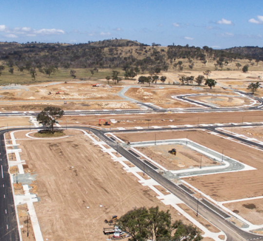 Image of land cleared ready for new buildings. Streets are paved and there are a couple of larger trees.