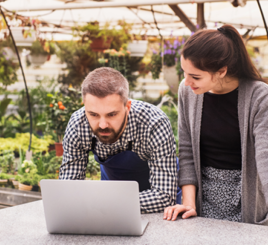 Man and woman looking at a laptop in a greenhouse environment.