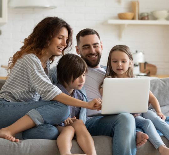 Happy family sitting on a couch using internet device laptop.