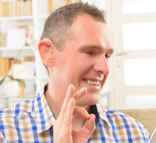 Smiling man with hearing aid signing to someone he is chatting to on his tablet device/
