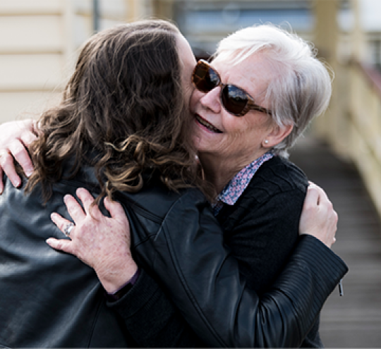Two people hug outside the ramp access of a town hall building. One is wearing sunglasses.