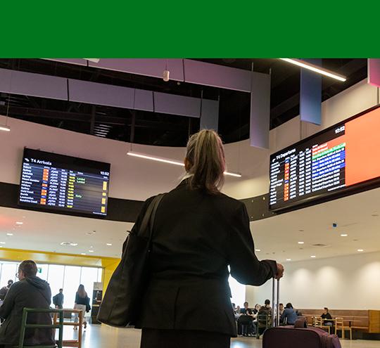 person looking up at flight information screens at an airport