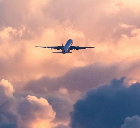 A passenger airplane silhouetted against sunset sky and clouds.