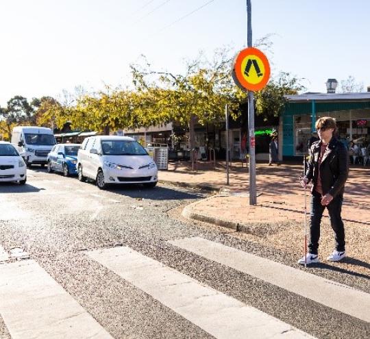 Man who is blind walking across a town centre crosswalk.