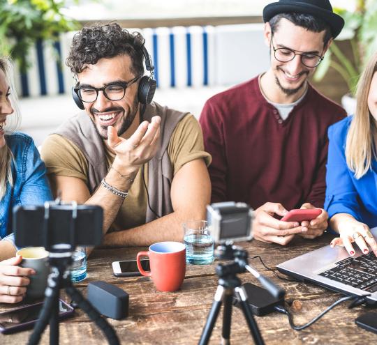 Young adults smiling and laughing sitting around streaming devices on a table.