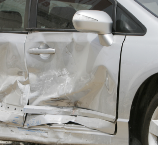 Silver car with a large dent in the side ruining two doors.
