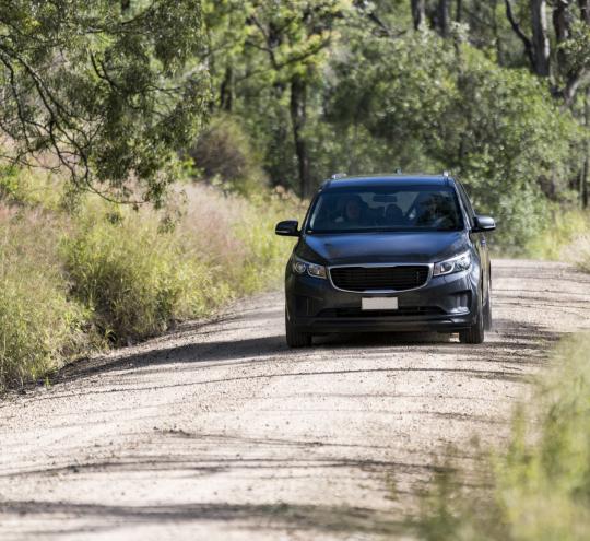 Image depicts a car driving on an unsealed road in a regional area.