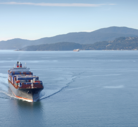 A freight carrier cruises through open water near land.