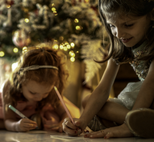 Children writing letters to Santa in front of a Christmas tree.