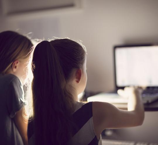 Image depicts two young girls using a computer).
