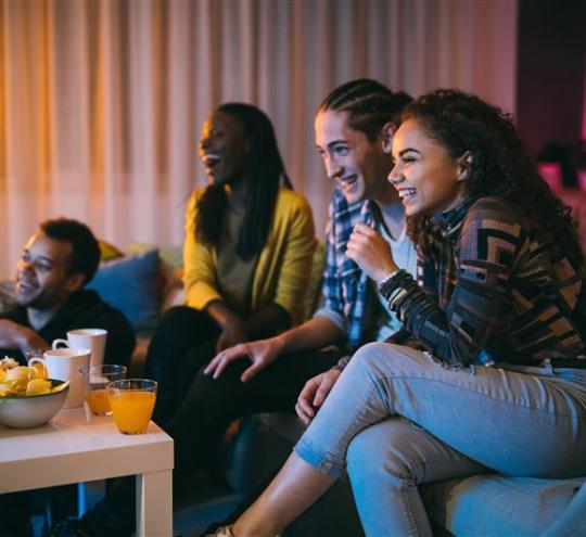 A group of young adults sitting on a couch watching a television which is just out of shot.