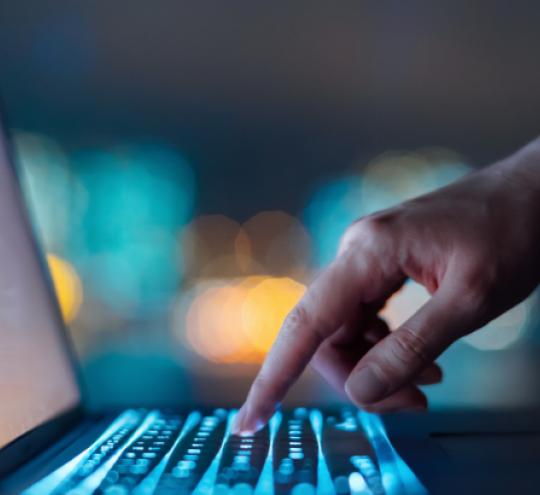 A hand touches a laptop keyboard in a dark room.