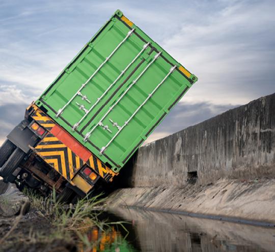 A green truck has tipped against a concrete wall