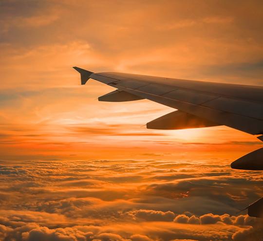 airplane wing flying over clouds at sunrise