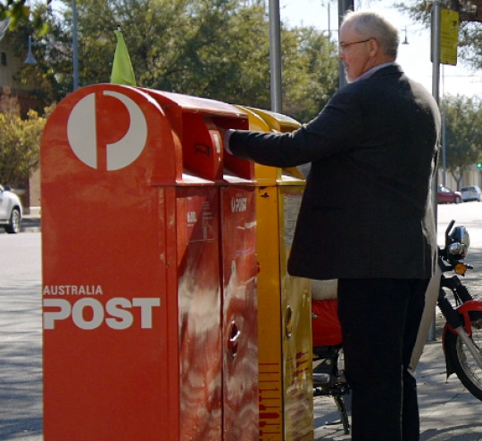 person posting letter at an Australia Post mailbox