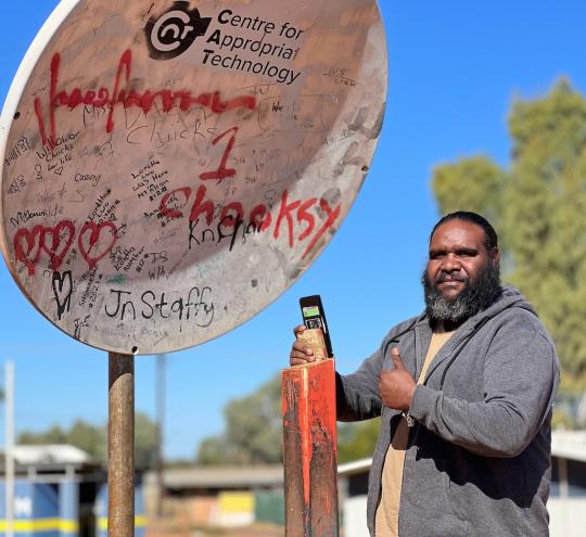Image of co-researcher Mel Langdon using the CAT mobile hotspot in Yuelamu, which enables access to the mobile signal from Yuendumu 43km away.