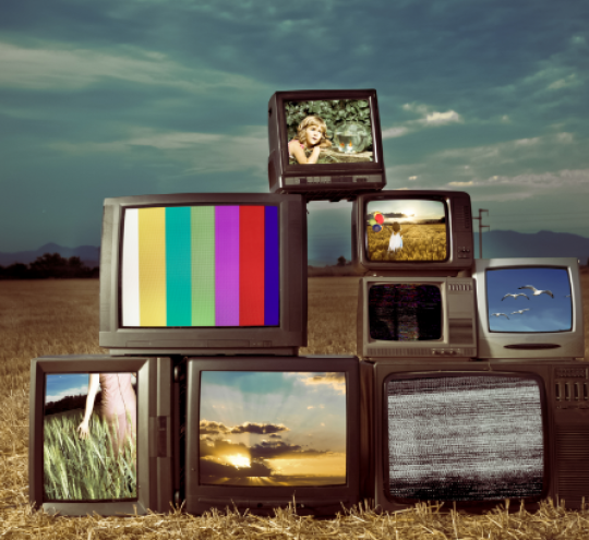 Several television sets showing various images sit in an open field 