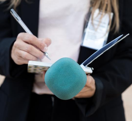 Journalist holding a microphone, notepad and pen.