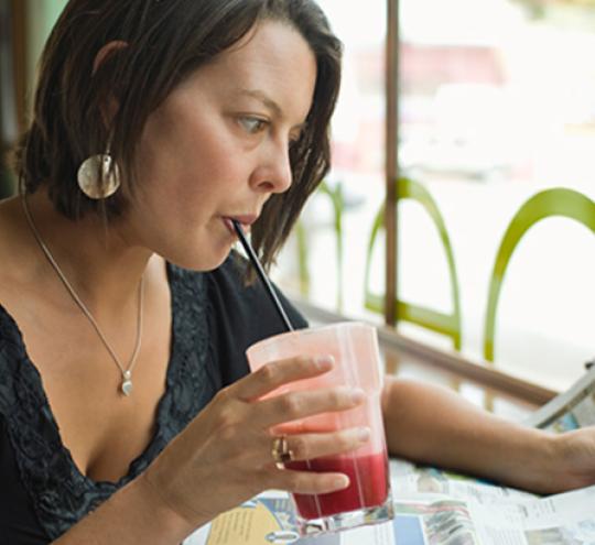 Woman drinking beverage and reading newspaper in a café.