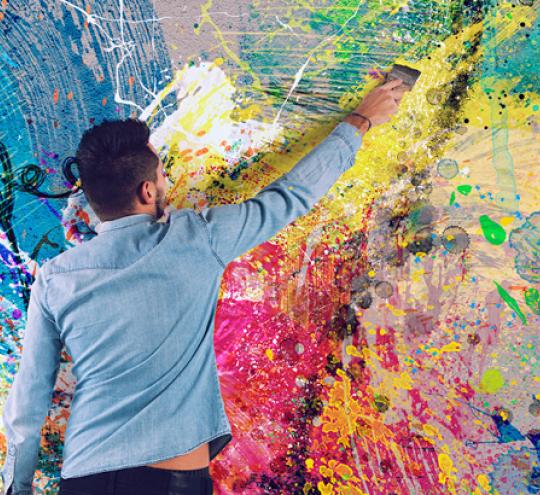 Man paints a big and colourful light bulb on a wall.