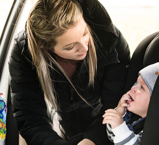Parent, mother, straps baby into rear child seat in car.