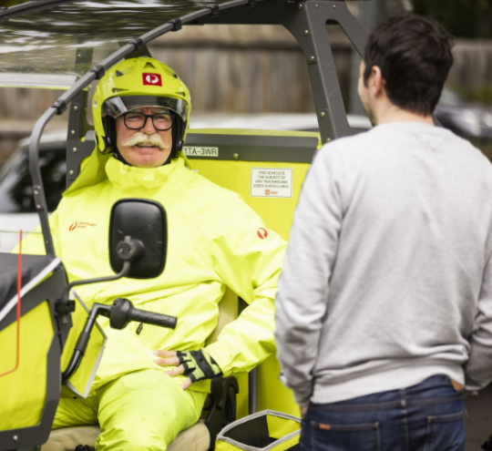 A postie in a postie vehicle chatting to a man on the street.