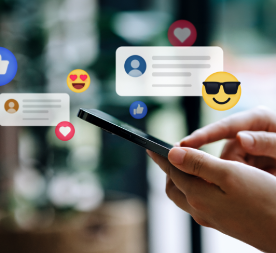 Hands holding smart phone, with emojis and social media comments floating above