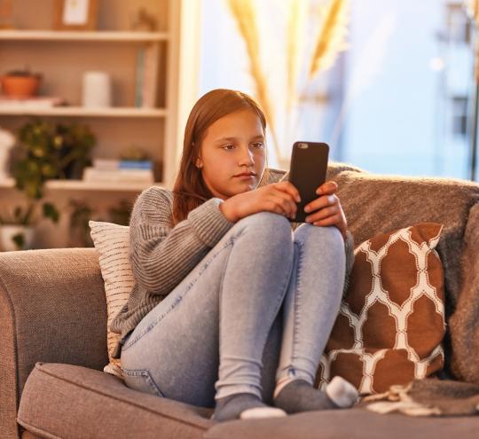 Teen girl sits on couch while browsing on her phone
