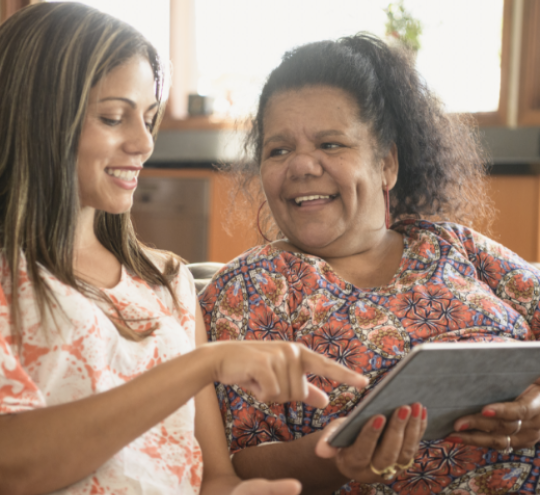 First Nations mother and daughter sitting on sofa at home pointing at a tablet