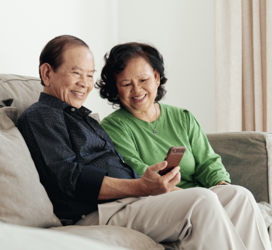 Two people sitting on a couch looking at a mobile phone 