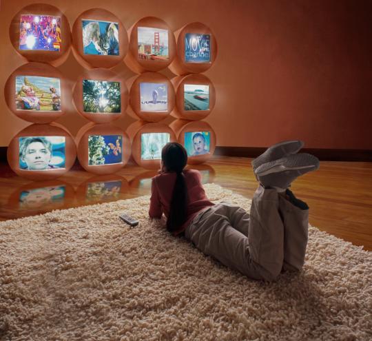 Young person lying on a rug and looking up at a wall of futuristic screens.