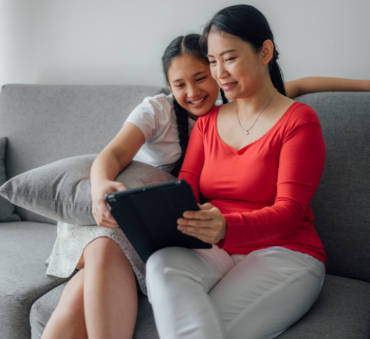 Seated person shows laptop to the teenager sat next to them.