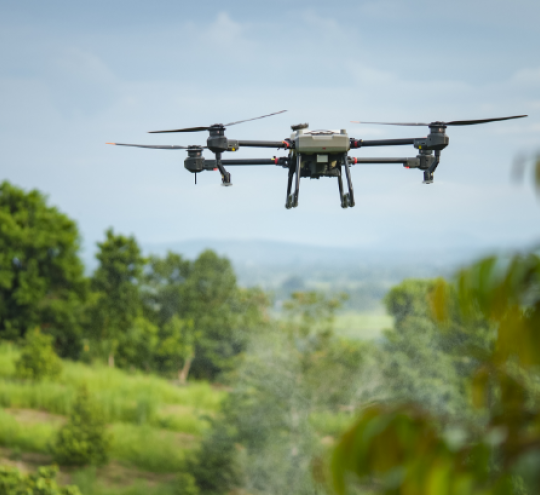 A drone in flight over a green landscape.