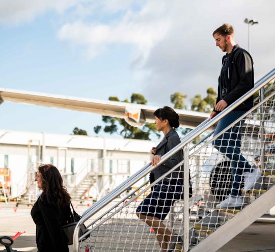 Image depicts passengers coming down the stairs from an airplane.