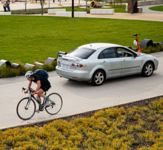 Person on bike, a car and an electric scooter on a path/drive.