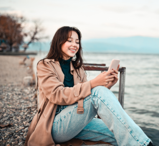 Women sitting on the edge of a pier looking at her mobile phone