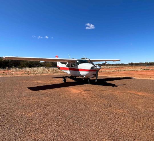 A small plane sitting on a landing strip in a remote area surrounded by red earth.