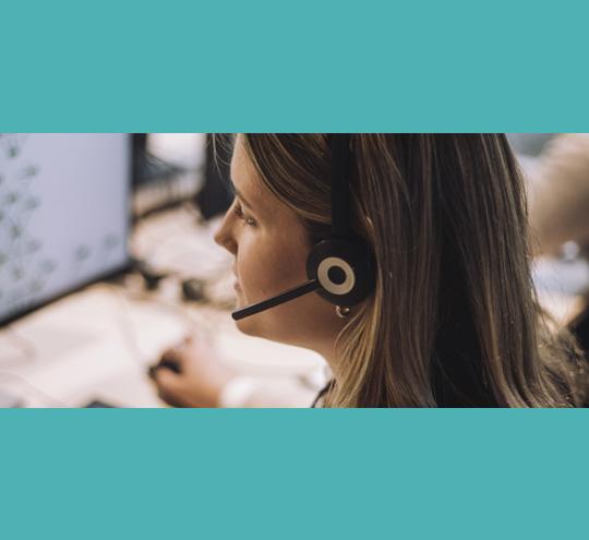 Person wearing a headset speaking into a microphone while using a computer in a call centre setting