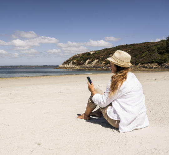 Woman using mobile phone on a beach on a sunny day.