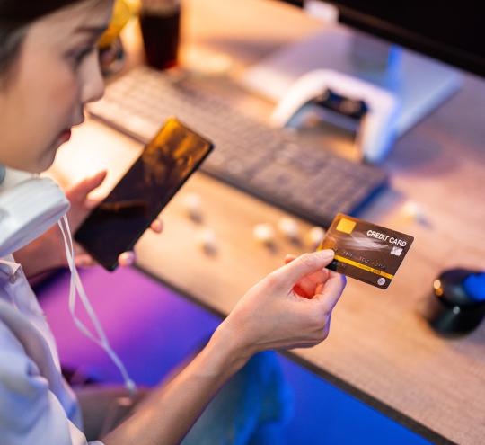 Image depicts person holding credit card while using phone.