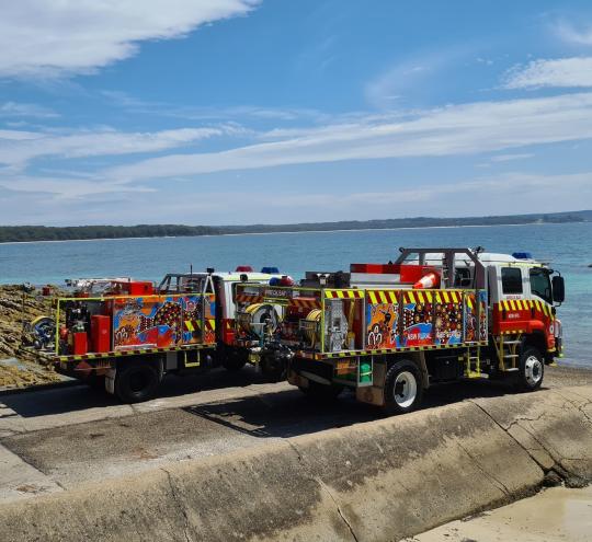 Two fire trucks sitting beside a body of water.