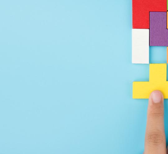 Finger pushing a jigsaw piece in to match the rest of the jigsaw pieces.
