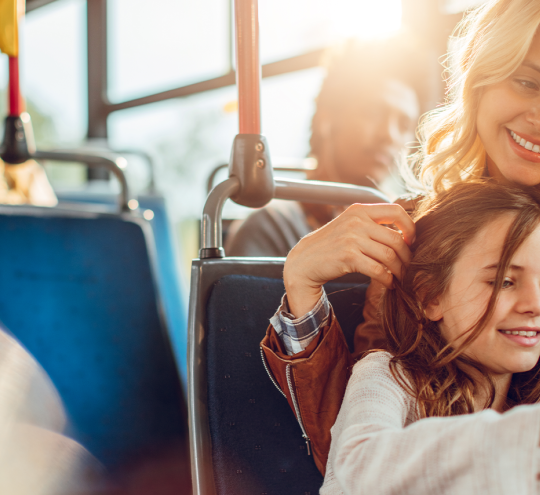  A mother and child are sitting in a bus looking at a phone together.