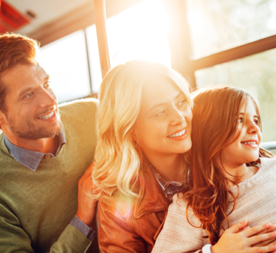 Parents with child on a bus. They are all looking out the window.
