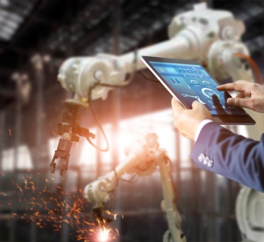 Man using a tablet in a factory to operate mechanical arms to do some welding work.