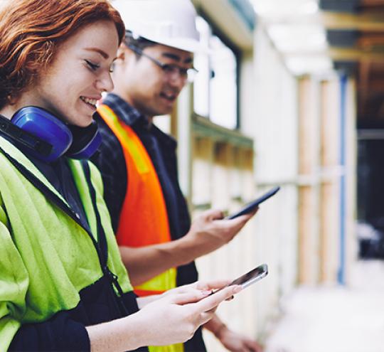 Woman and male tradies on a building site using mobile devices.